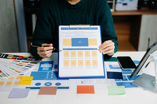 Persona mostrando un diseño web impreso para evaluar habilidades en maquetación