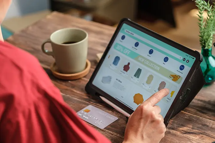A person browsing an online store on a tablet, selecting fashion products with a card at hand.